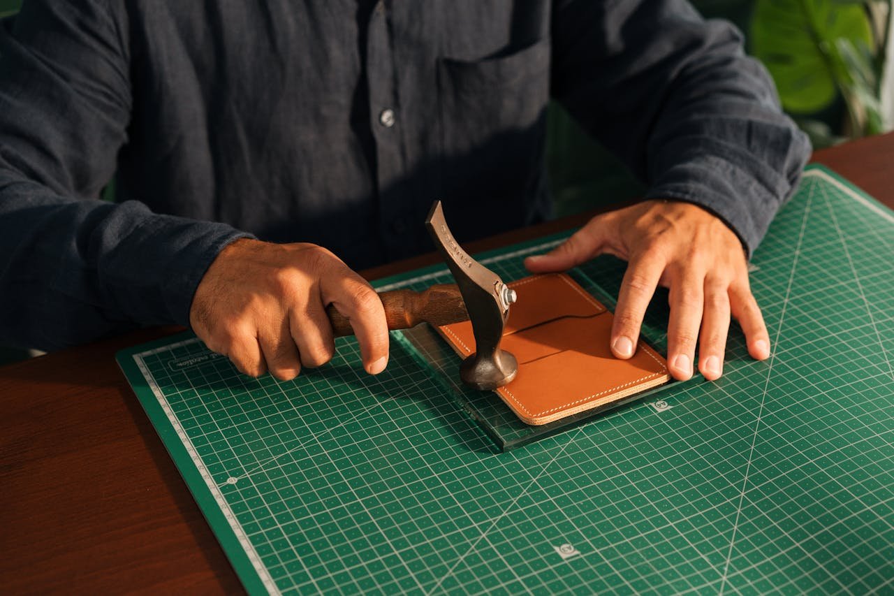 Home Artisan precisely crafting leather product with hand tools on cutting mat.