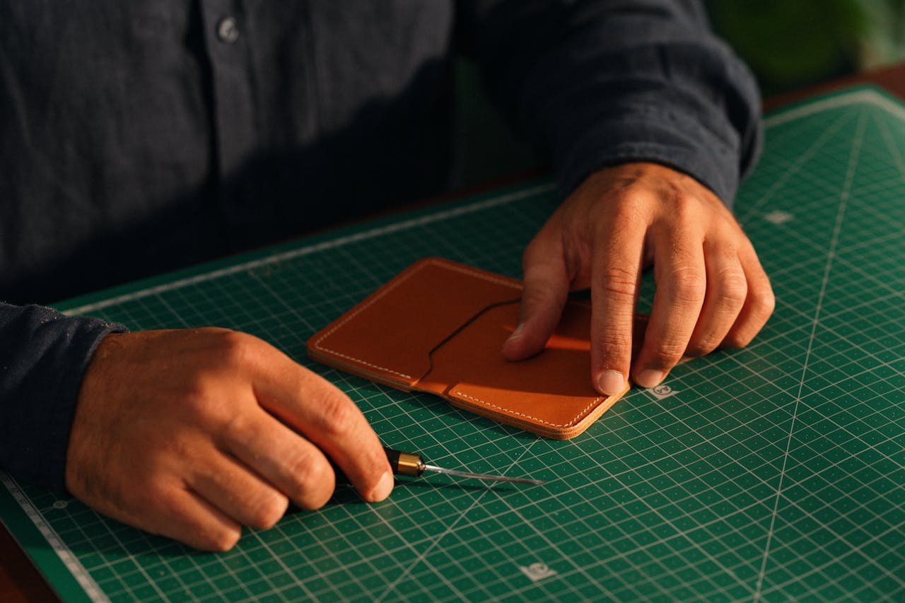Home Close-up of hands crafting a leather wallet on a green cutting mat, emphasizing artisanal craftsmanship.
