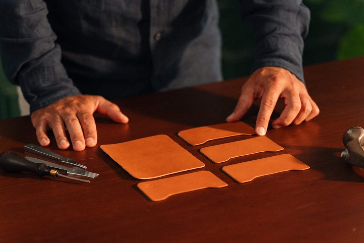 Home Hands of a craftsman meticulously arranging leather pieces with tools on a wooden table.