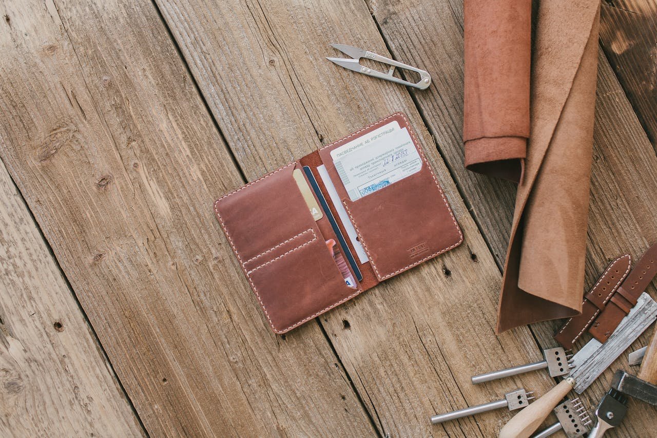 Services Brown leather wallet with accessories on wooden planks, featuring crafting tools and materials for leatherwork.