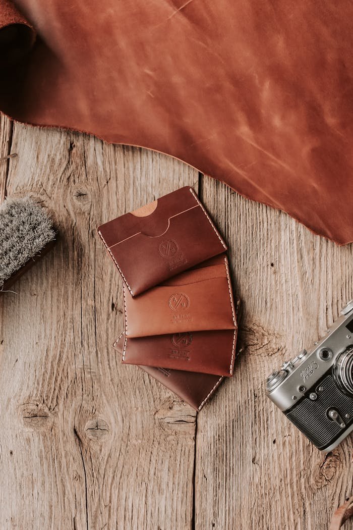 Services Flat lay of handcrafted leather wallets and vintage camera on rustic wooden surface.