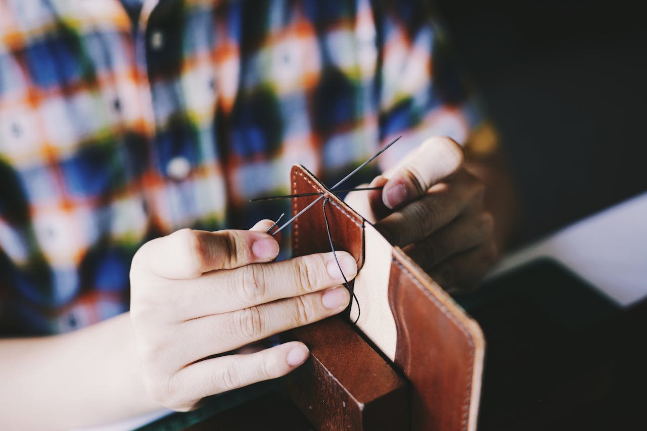 Home Close-up of a person hand-stitching leather, showcasing detailed craftsmanship and DIY skills.